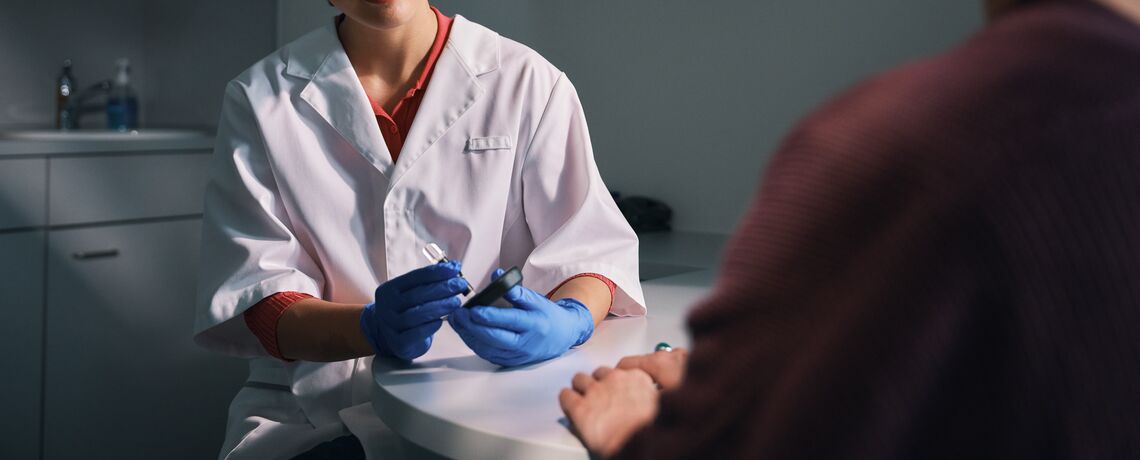 Un professionista con camice bianco e guanti blu esegue un DiabetoTest nell’ambito della Consulenza Plus presso Sun Store.